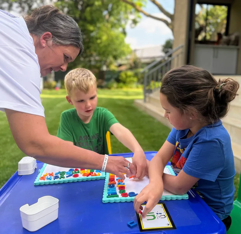 A Starbound educator guides two children as they build words with magnetic letters at an outdoor table