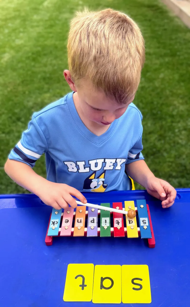 A boy taps out the sounds of the word “sat” on a letter xylophone